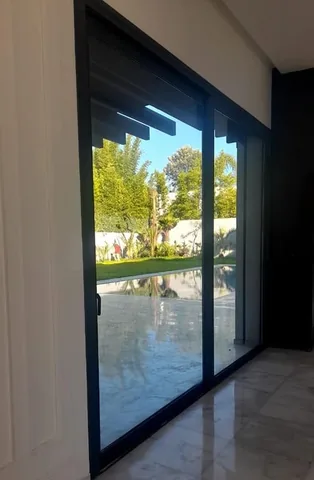Grande baie vitrée en aluminium noir donnant sur le jardin d'une villa, à Rabat
