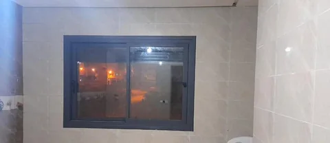 Fenêtre coulissante en aluminium noir posée dans une pièce carrelée, à Rabat